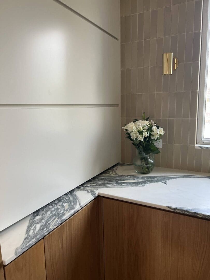 Modern kitchen corner with marble countertop and white flowers in a glass vase.