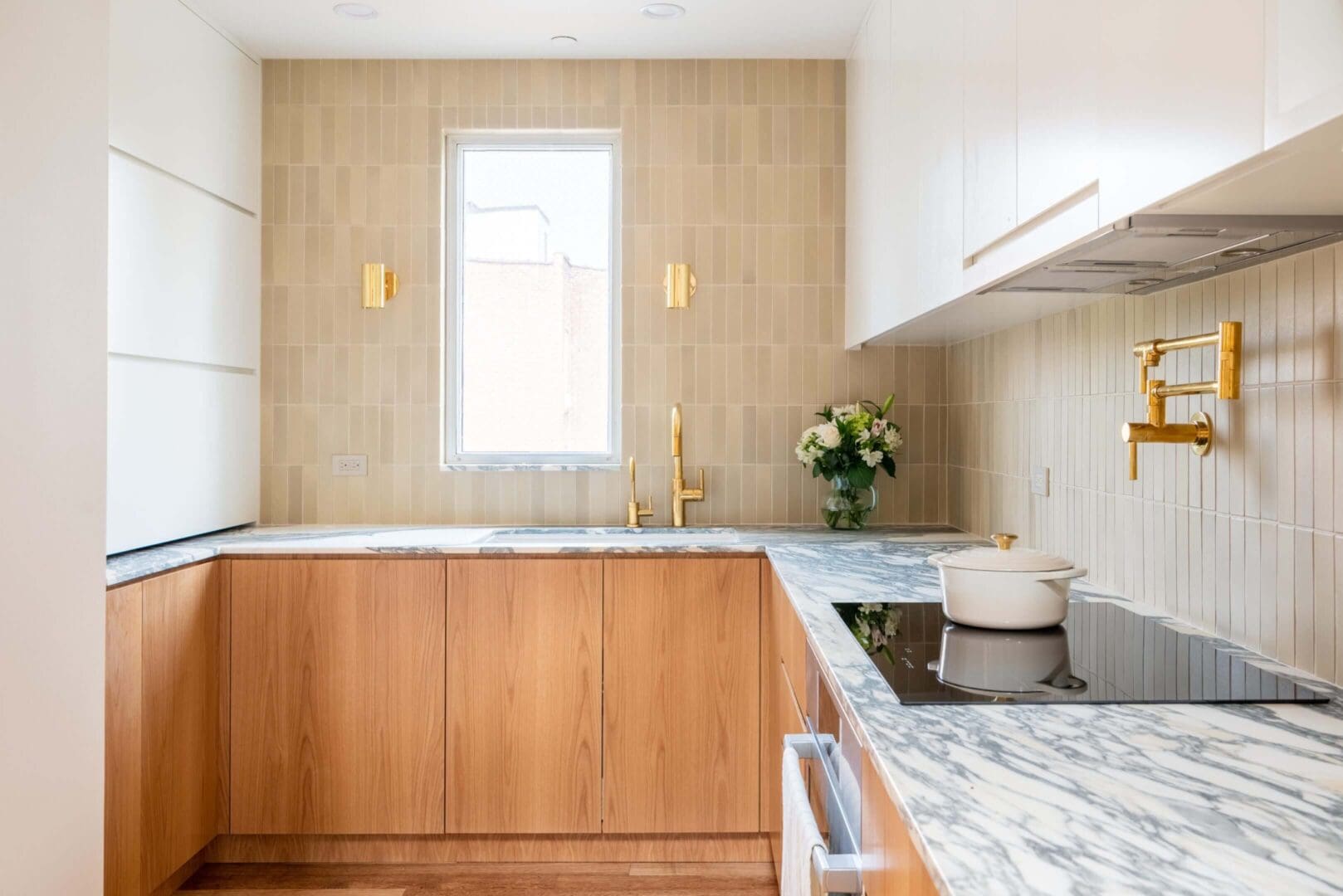 Modern kitchen with wooden cabinets and marble countertops under natural light.