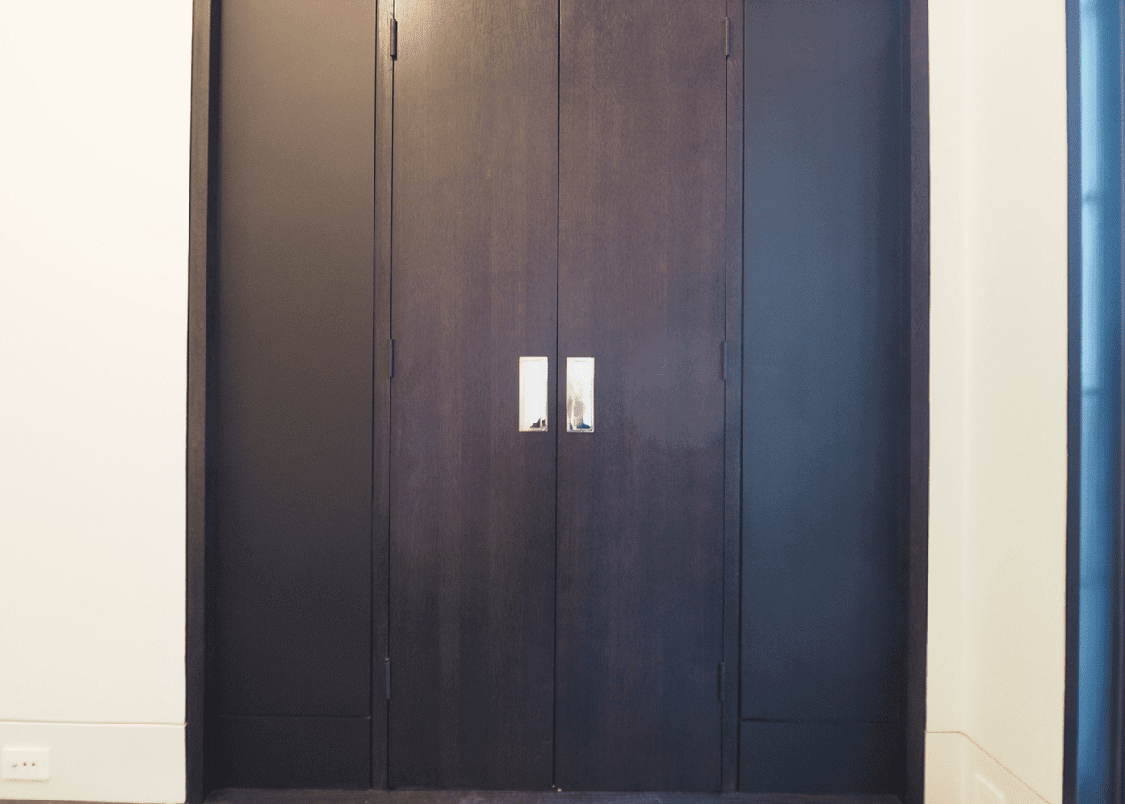 Tall black wardrobe with white handles against a plain wall.