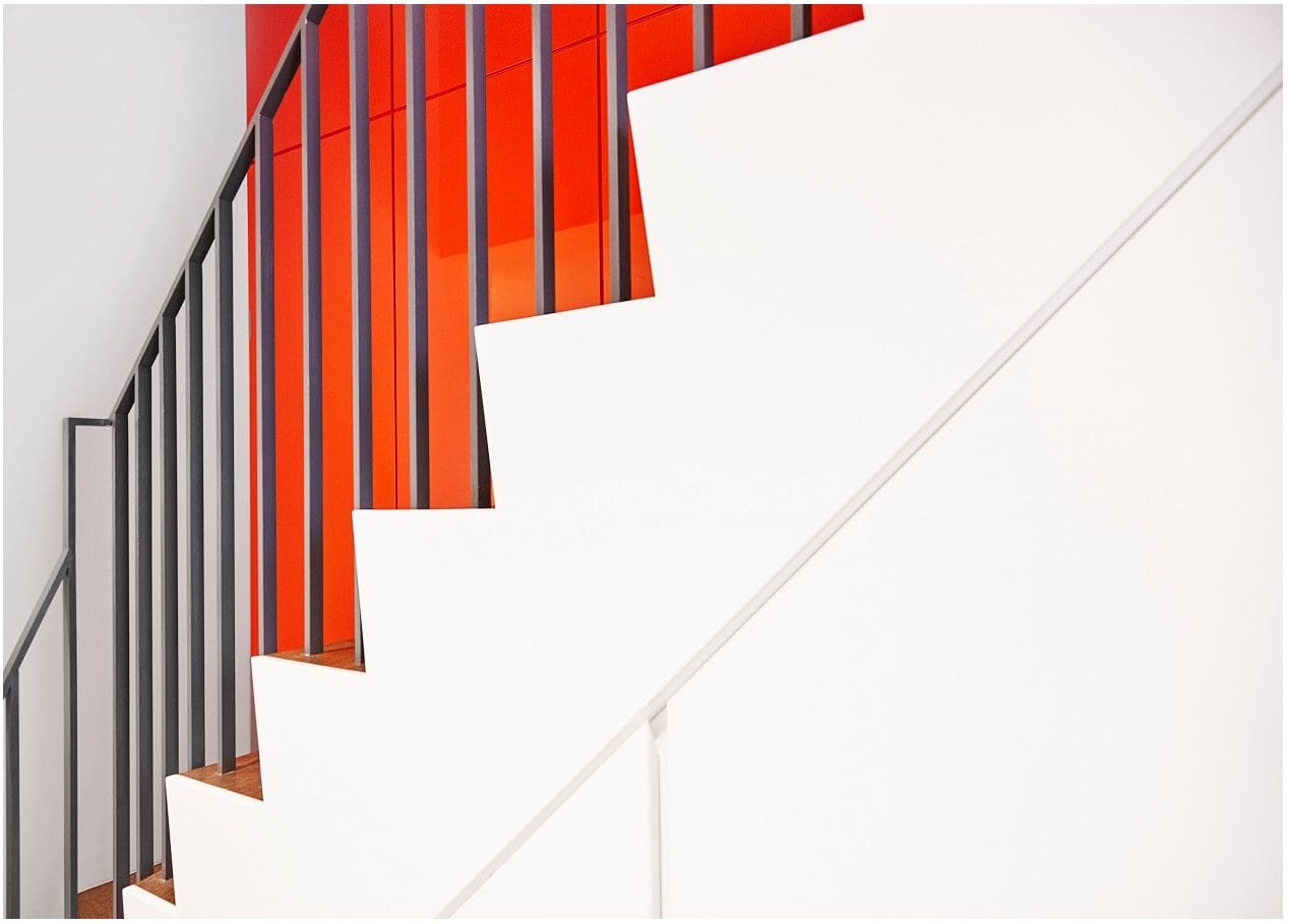 Modern white staircase with a bold red wall and black railing.