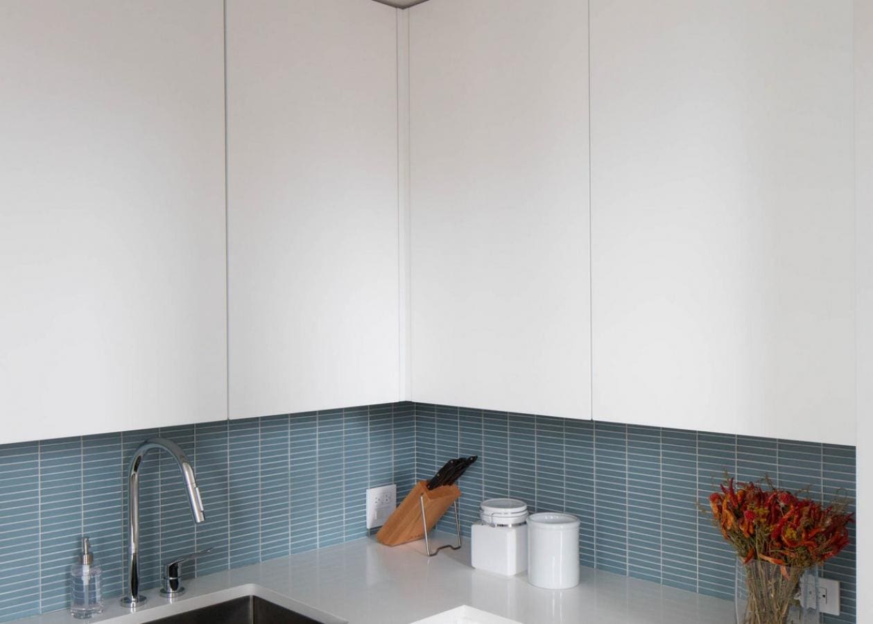 Modern kitchen corner with blue tiled backsplash and white cabinets.