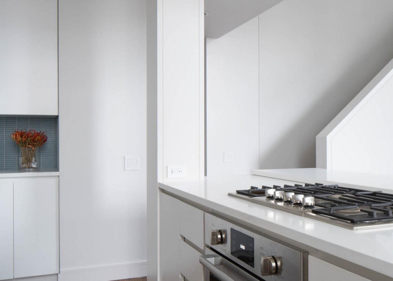 Modern kitchen corner with built-in oven and gas stove under a sleek white countertop.