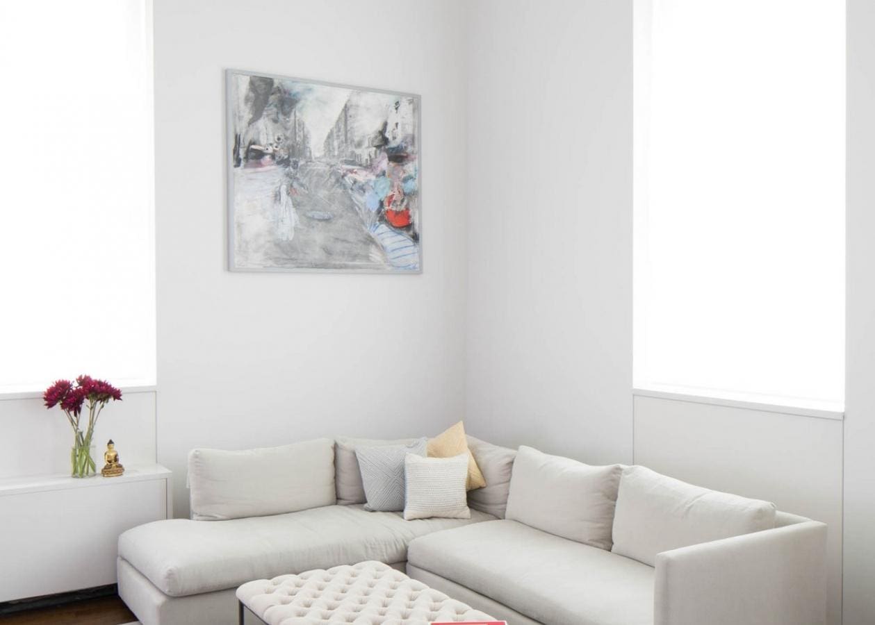 Modern living room with a light gray sectional sofa and colorful abstract wall art.