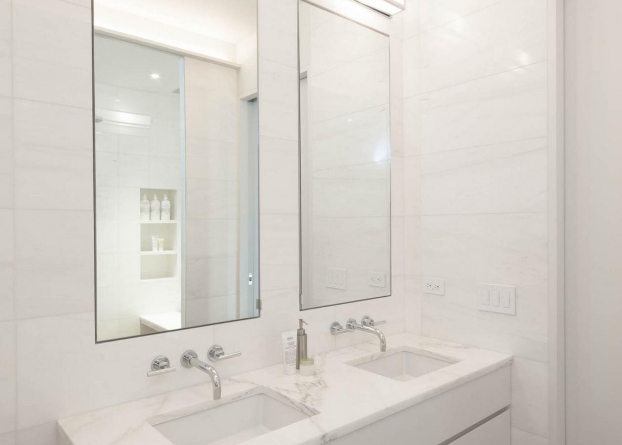 Modern white bathroom with dual sinks and large mirror.