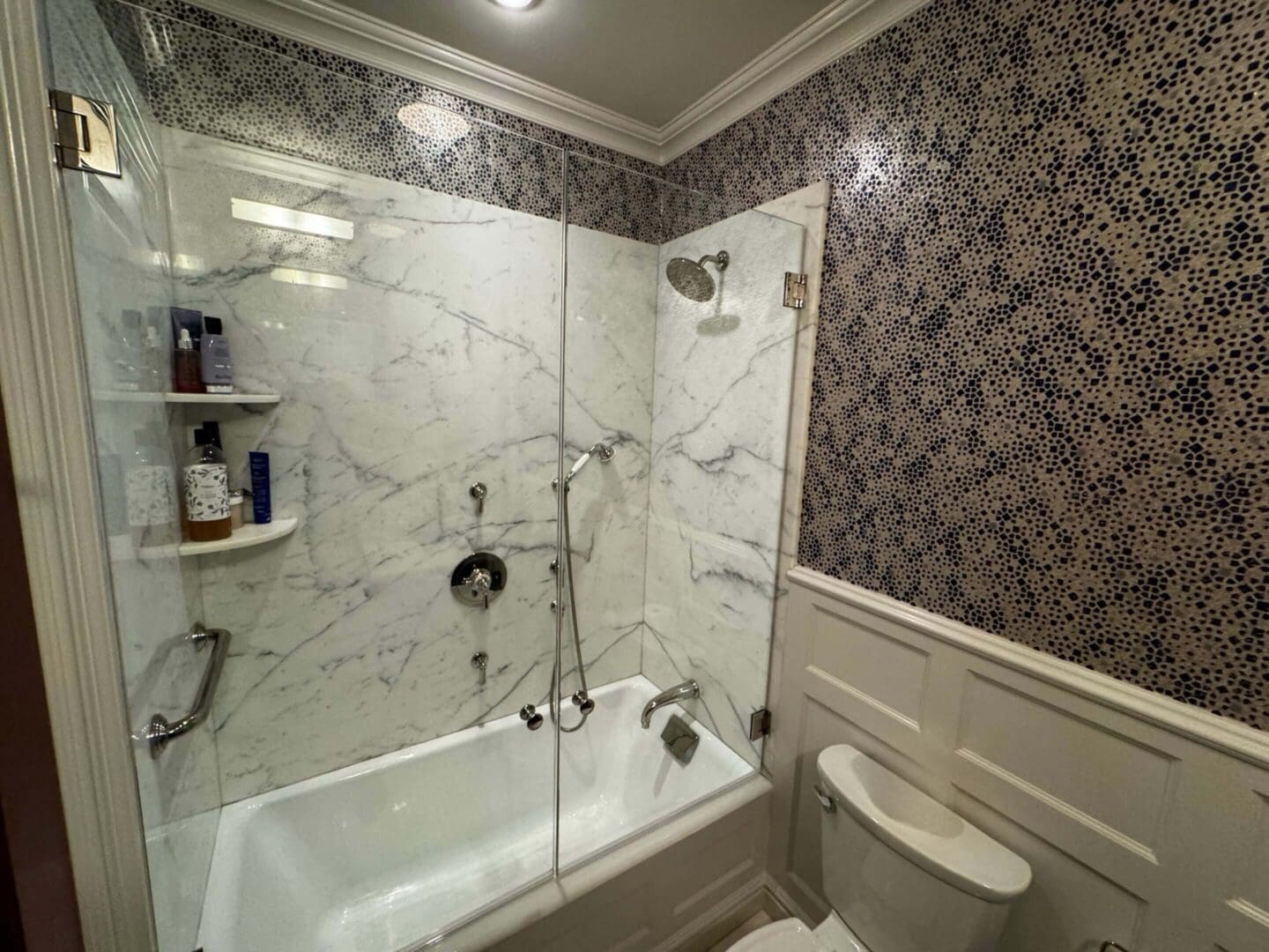 A bathroom with a bathtub, shower, and patterned wallpaper.