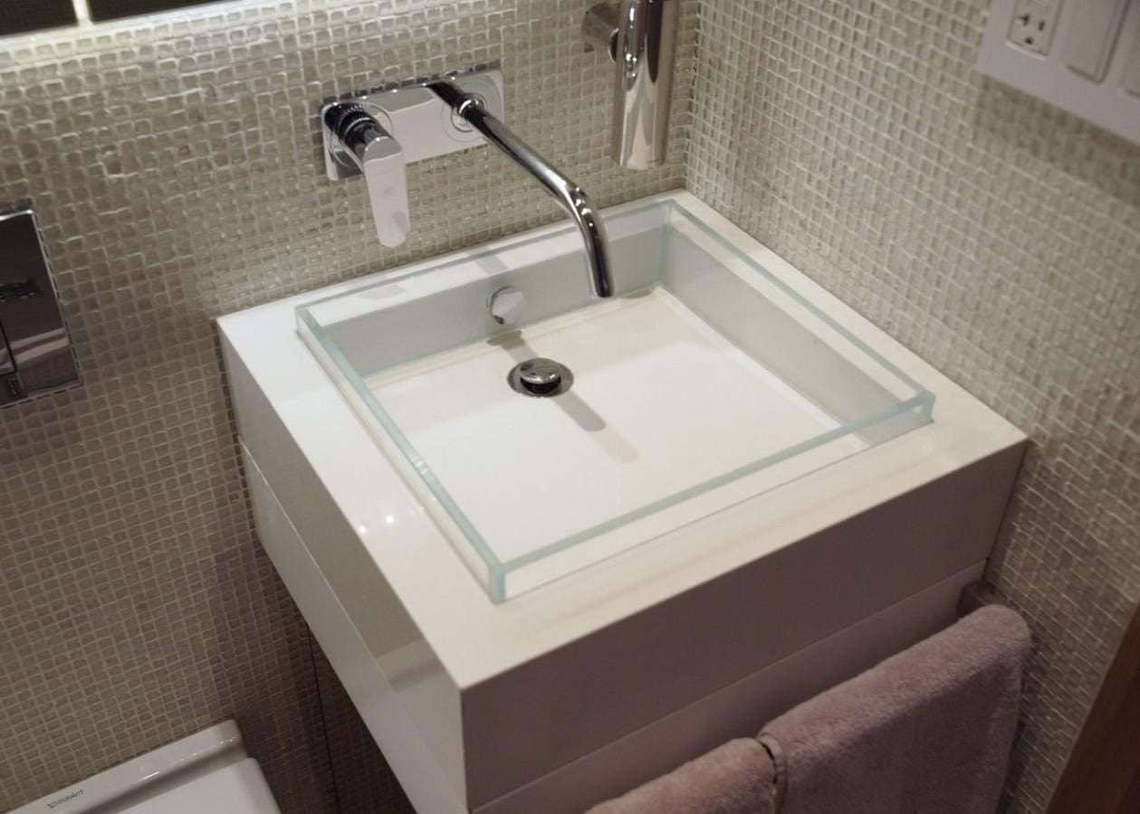 Modern square sink with glass countertop and wall-mounted faucet.