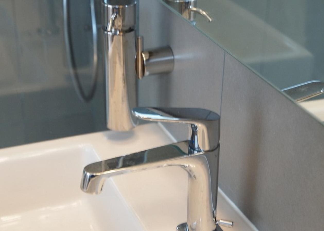 Modern chrome faucet installed on a white sink with tiled wall.