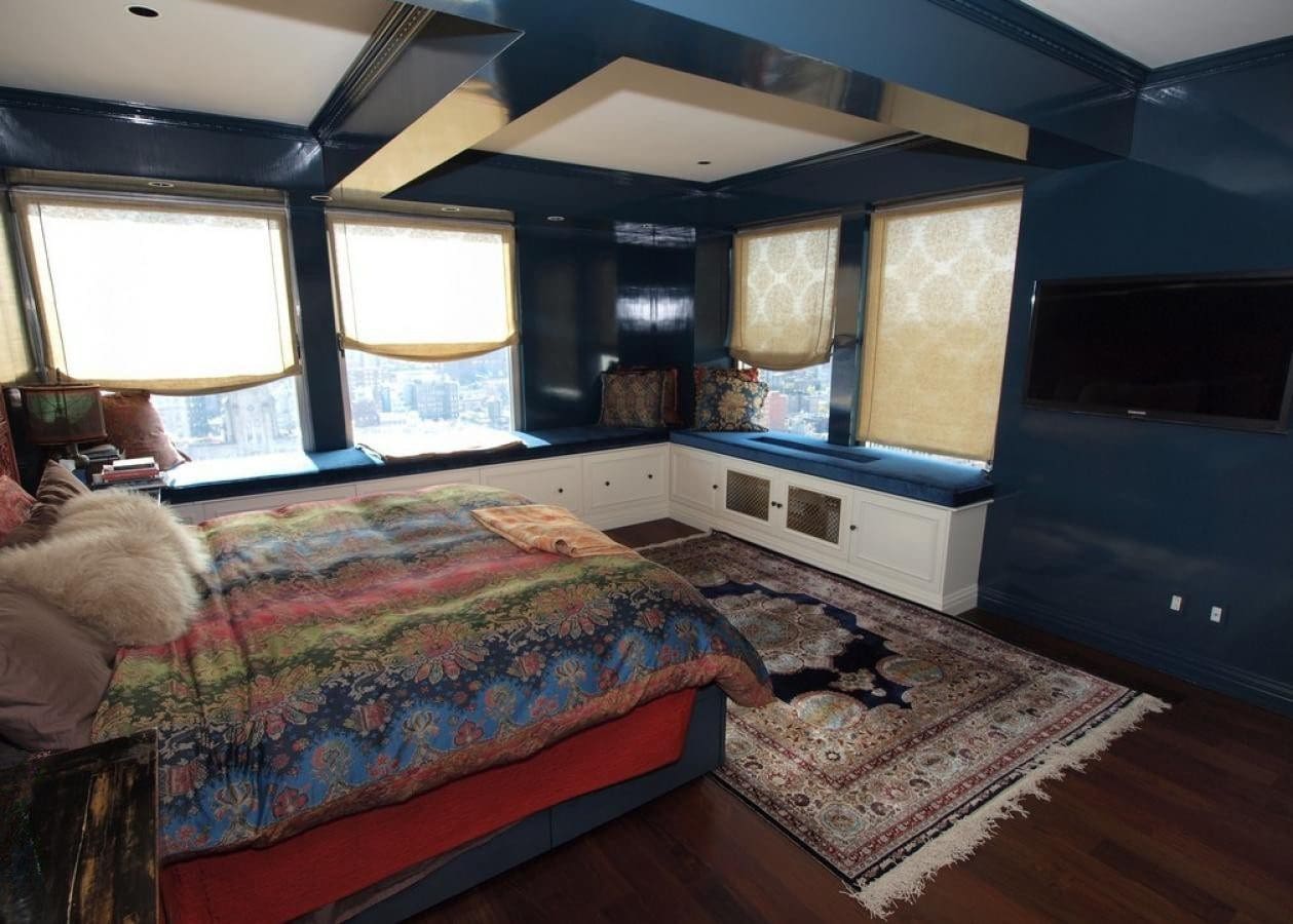 Cozy bedroom with colorful bedding, large windows, and a patterned rug.