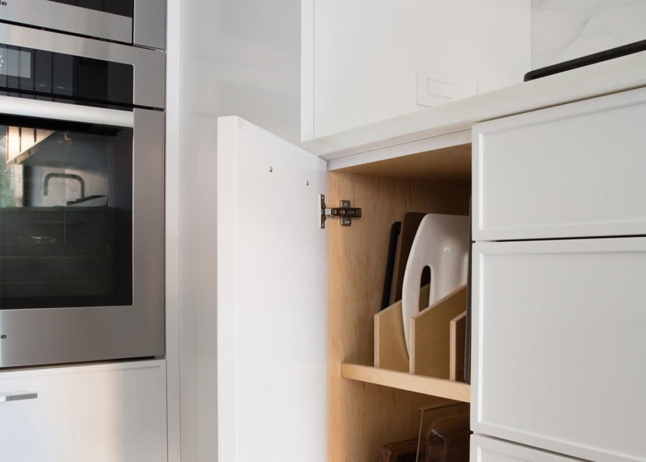 Open kitchen cabinet with organized cutting boards inside.