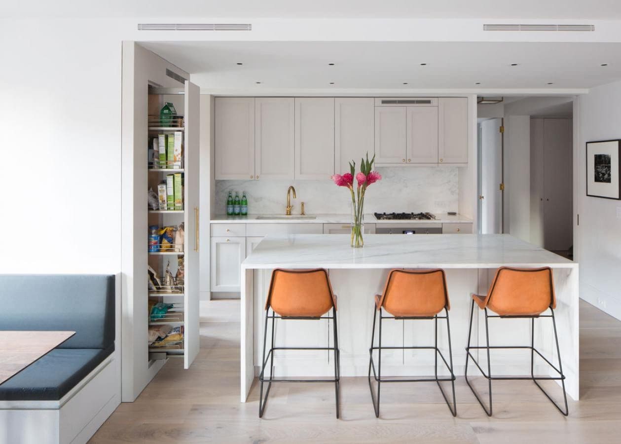 Modern kitchen with orange bar stools and white cabinetry.