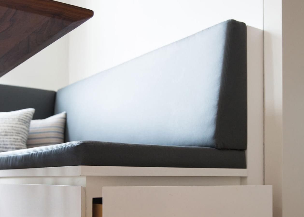 Minimalist corner bench seat with gray cushioning and white base.