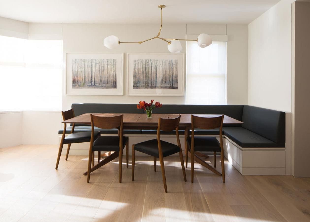 Modern dining room with wooden table, chairs, and black cushioned bench seating.