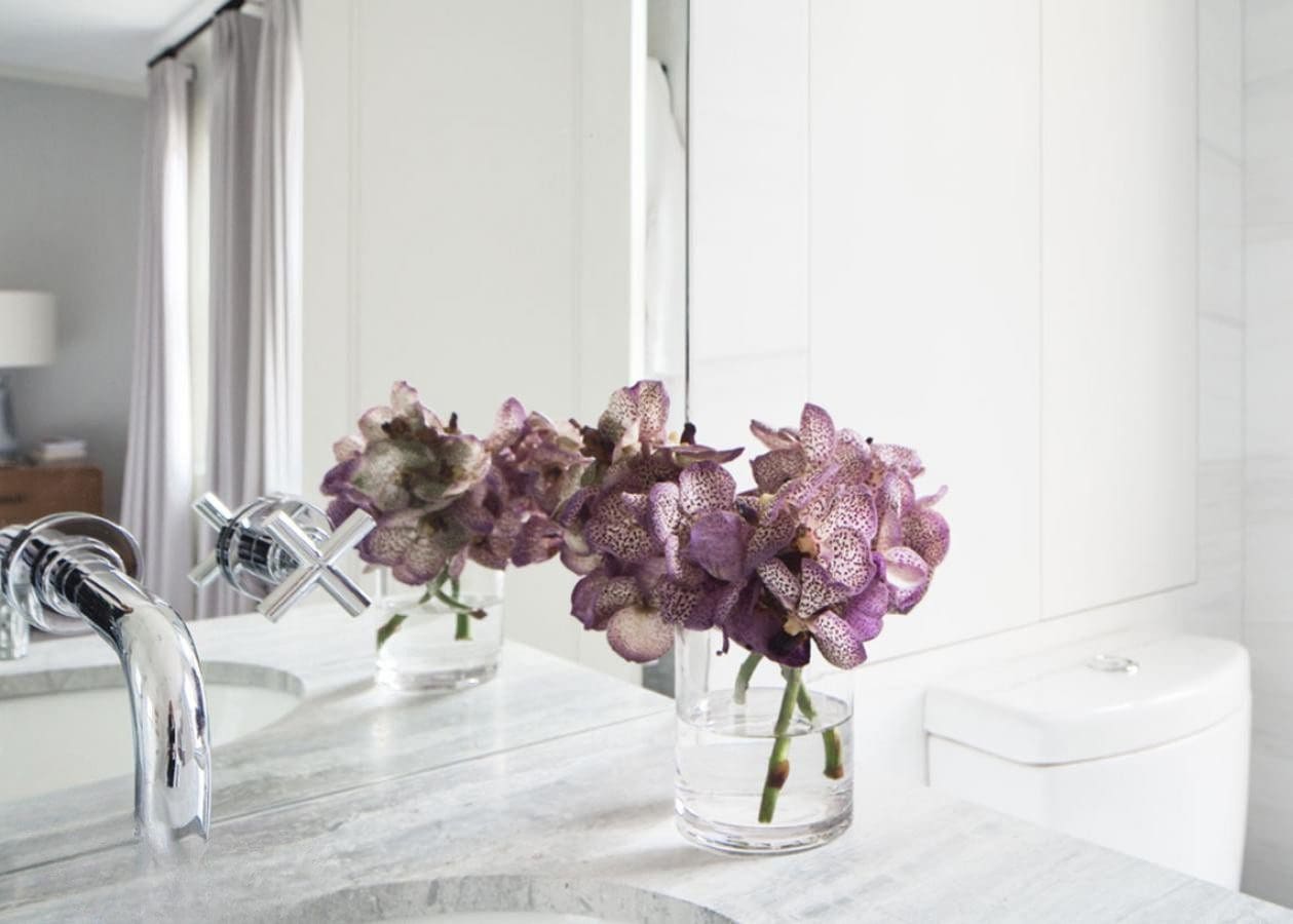 Delicate purple flowers in a glass jar on a bathroom sink.