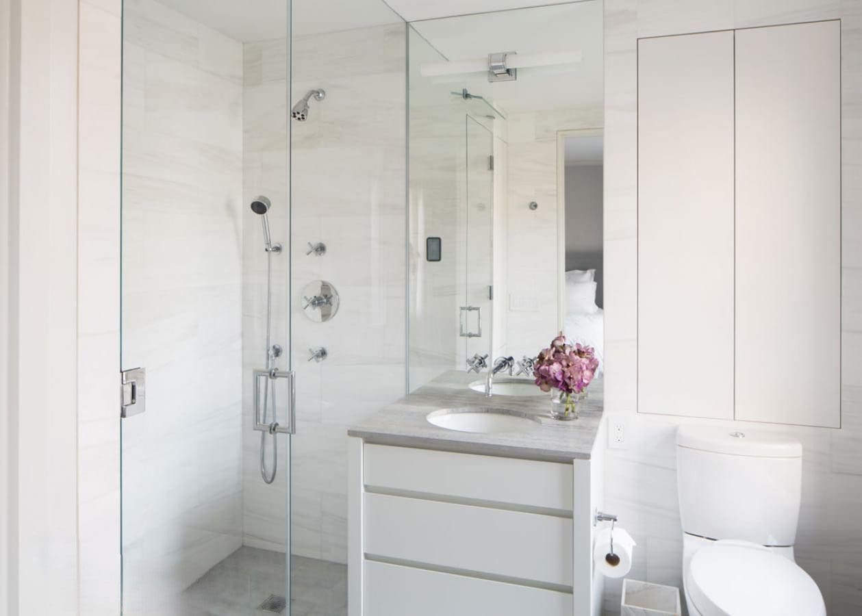 Modern white bathroom with glass shower enclosure and sleek vanity.